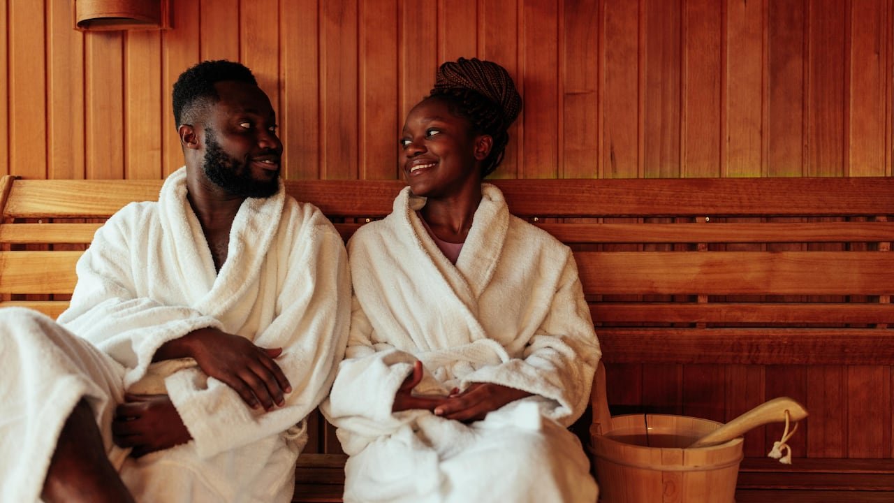 default-37 A couple in bath robes sitting in a sauna, smiling at each other.