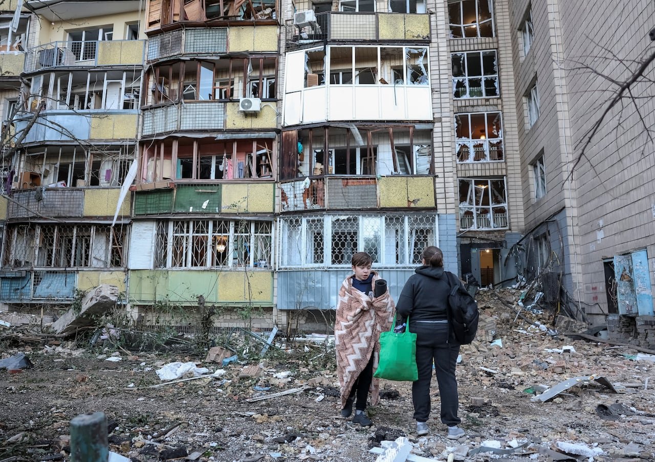 default-465 A boy wrapped in a blanket stands outside a damaged apartment building beside another resident.